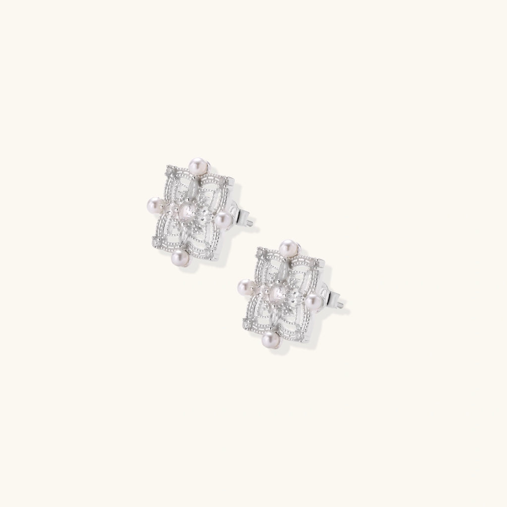 Ornate sterling silver stud earrings with mandala-inspired filigree pattern and four freshwater pearls on beige background