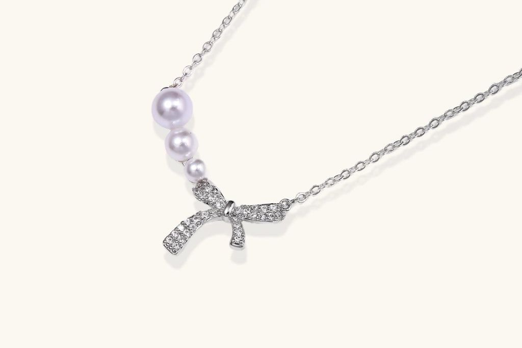 Delicate white gold plated necklace with freshwater pearls and sparkly crystal bow pendant on white background