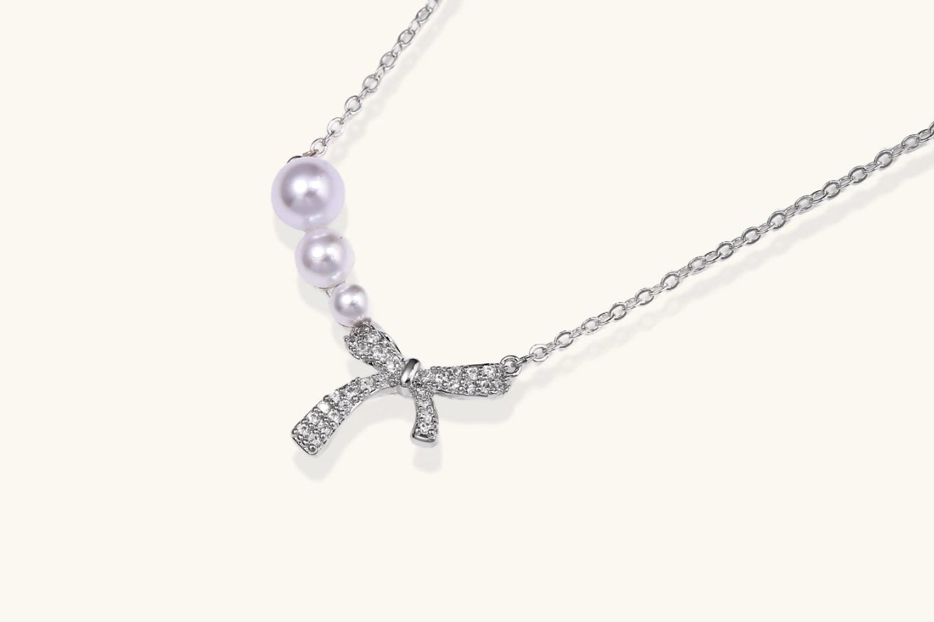 Delicate white gold plated necklace with freshwater pearls and sparkly crystal bow pendant on white background